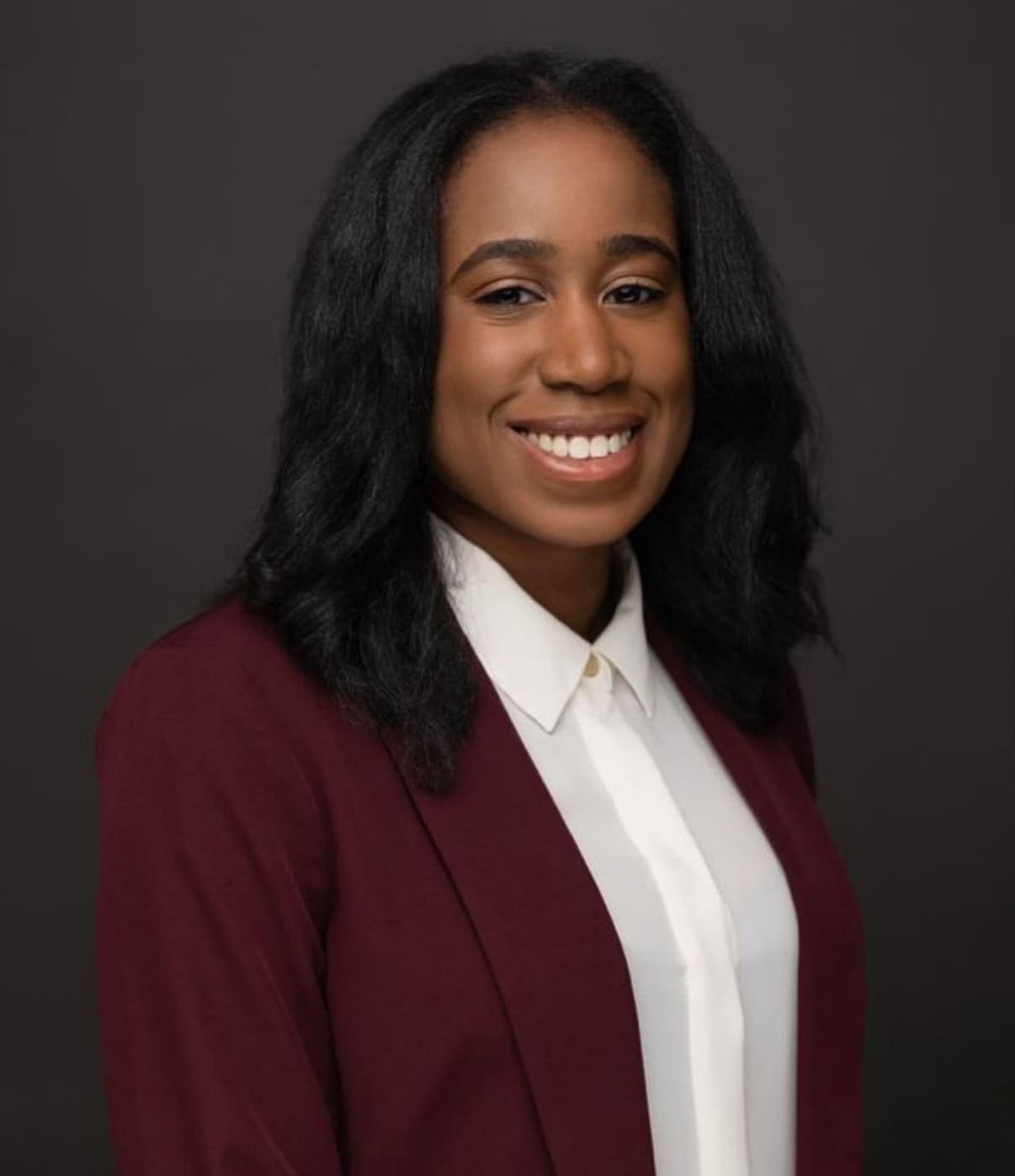 Dr. Chinwendu Uzosike, smiling in a professional maroon blazer and white blouse, against a dark background, representing compassionate dental care at Toothfully Yours in Owings Mills, MD.