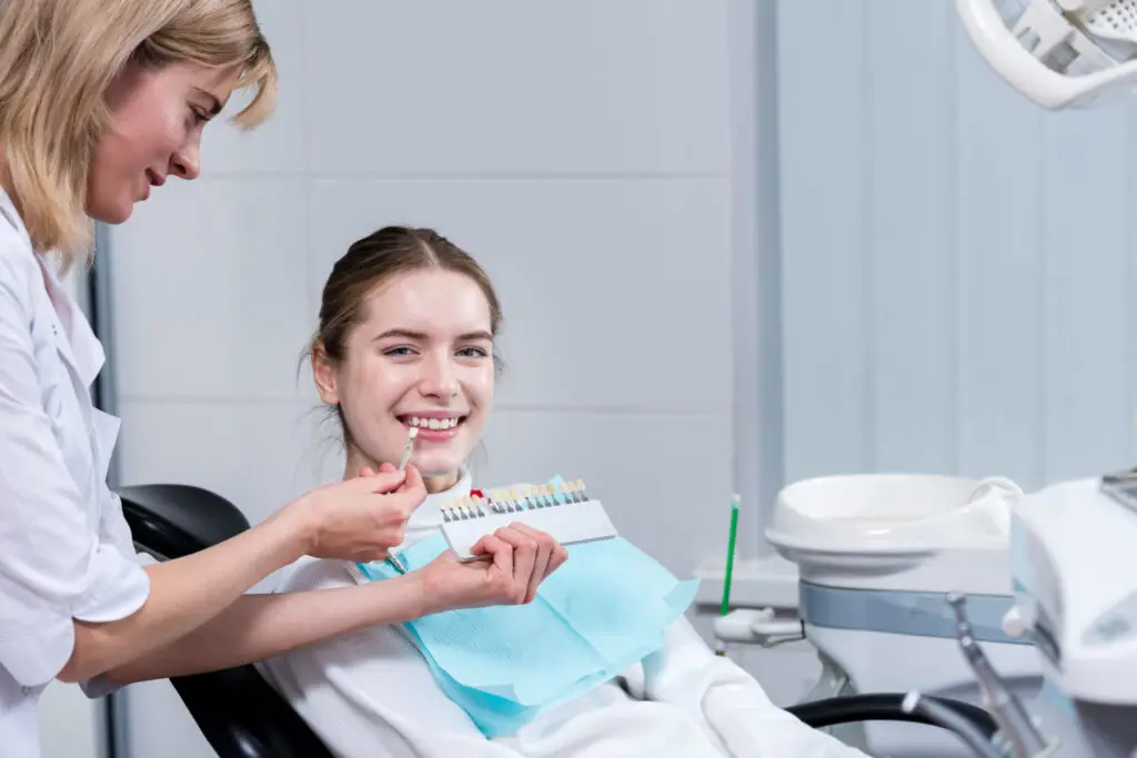 Dentist comparing porcelain veneer shades with a smiling patient during a cosmetic dentistry consultation for veneer treatment.