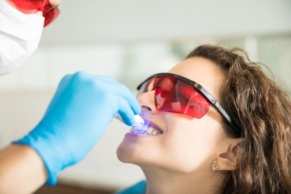 Patient undergoing professional in-office teeth whitening treatment with protective eyewear and LED whitening light in Owings Mills.