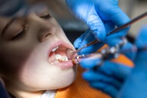 Dentist examining a childโs teeth with dental instruments during a routine dental checkup.